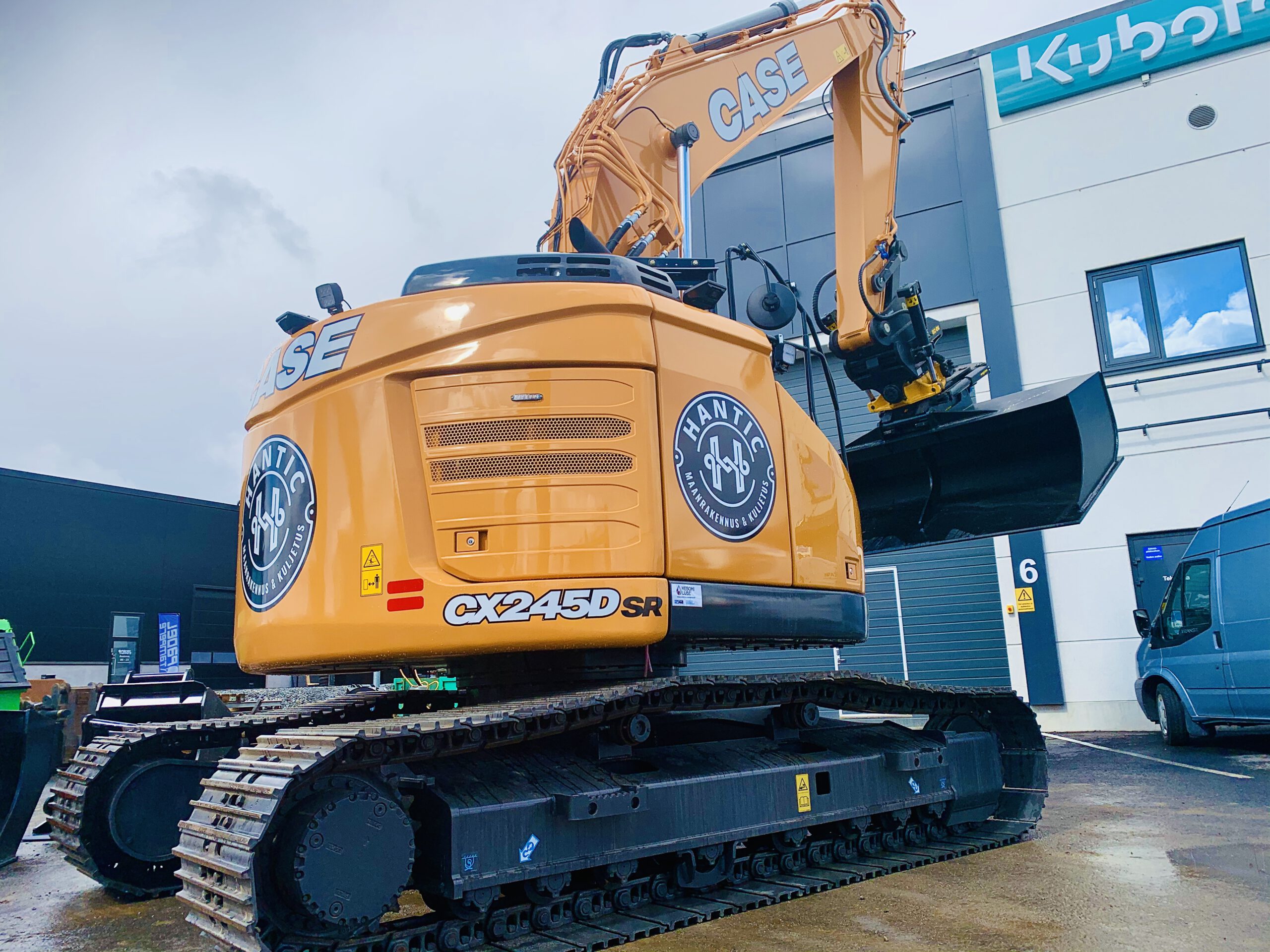 Oranssi CASE CX245D SR -kaivinkone mustilla teloilla ja kauhalla, pysäköitynä rakennuksen edessä.