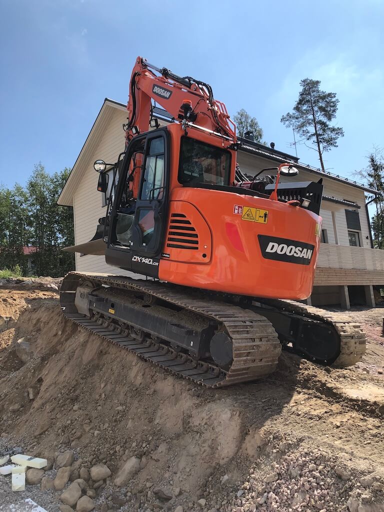 Oranssi Doosan-kaivinkone työmaalla talon edessä aurinkoisena päivänä.