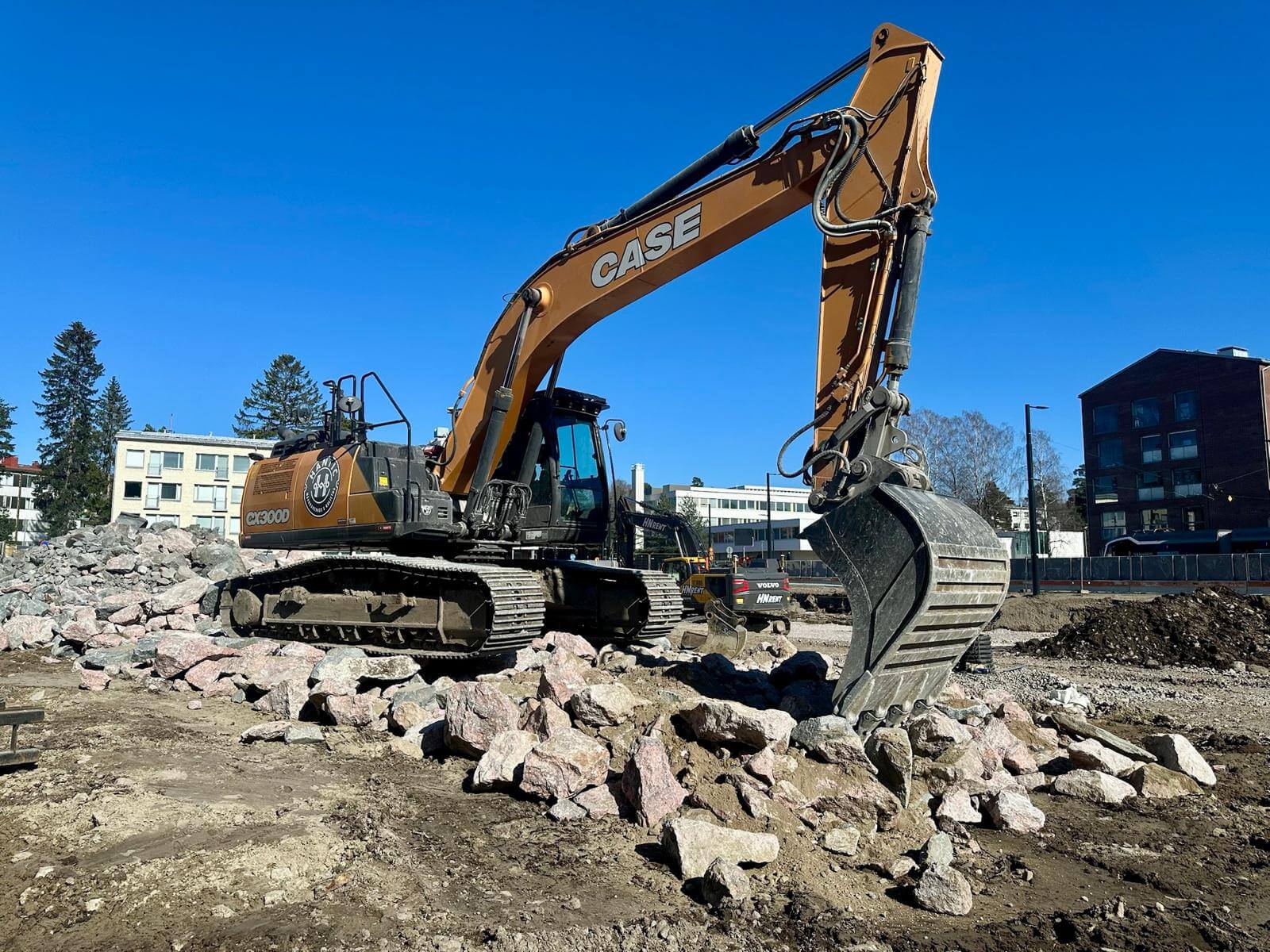 Kaivinkone työmaalla kasa kivikasoja siirtämässä aurinkoisena päivänä.