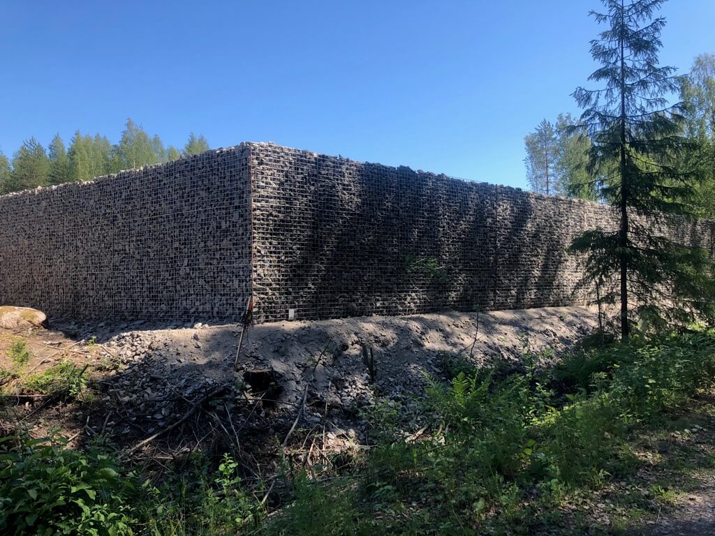 Korkea kiviverkosta rakennettu muuri metsässä kirkkaan sinisen taivaan alla.