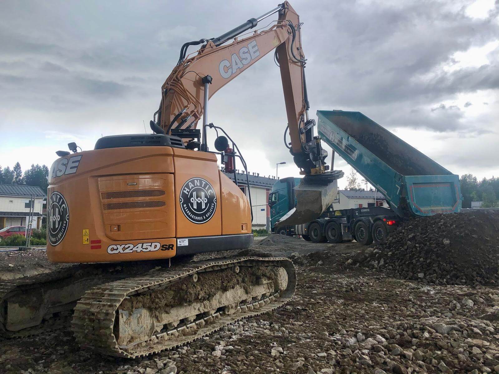 Kaivinkone lastaa maata siniseen kuorma-auton perävaunuun rakennustyömaalla.