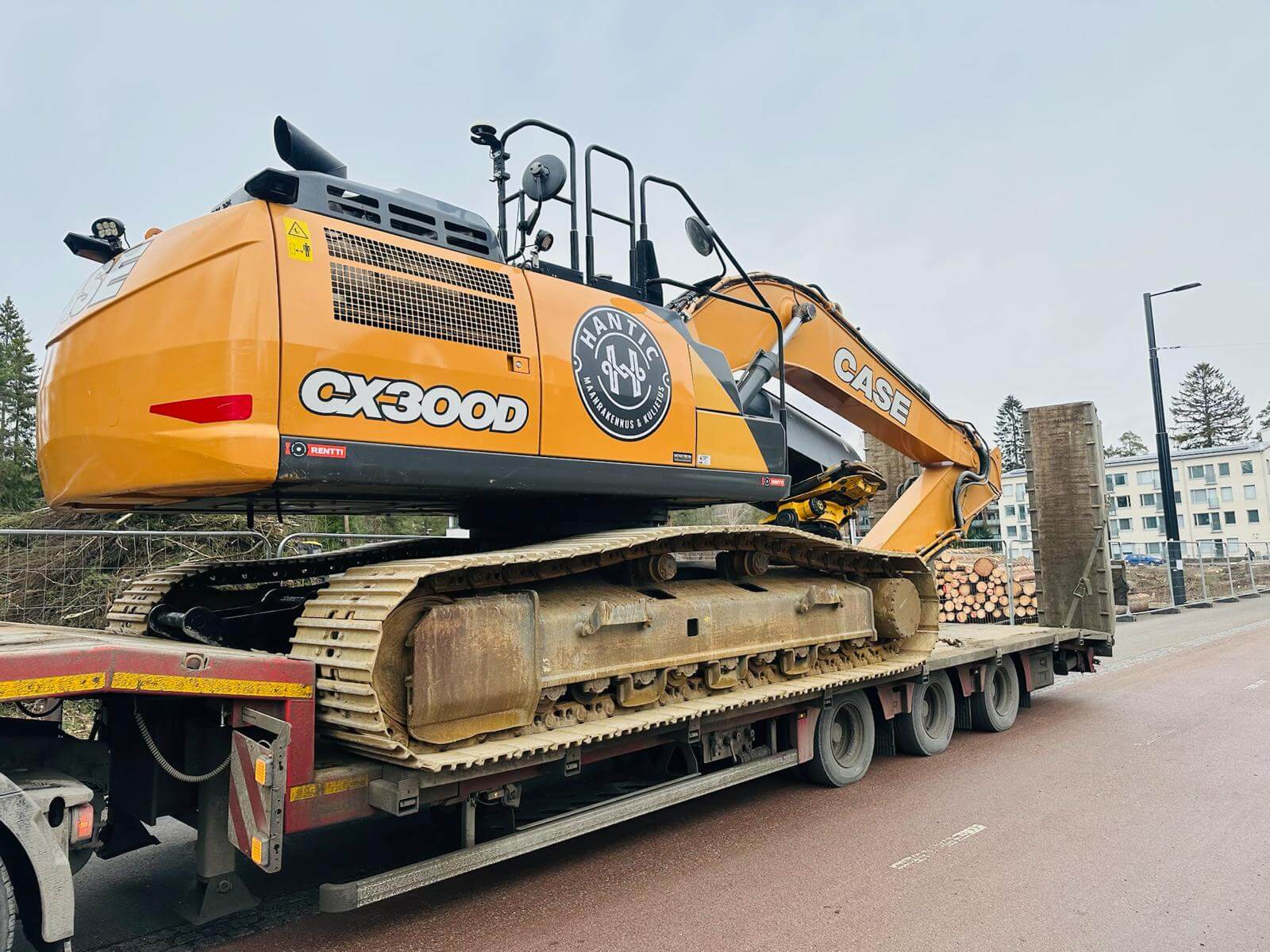 Oranssi CASE CX300D -kaivuri lastattuna puoliperävaunuun, taustalla taloja ja puita.