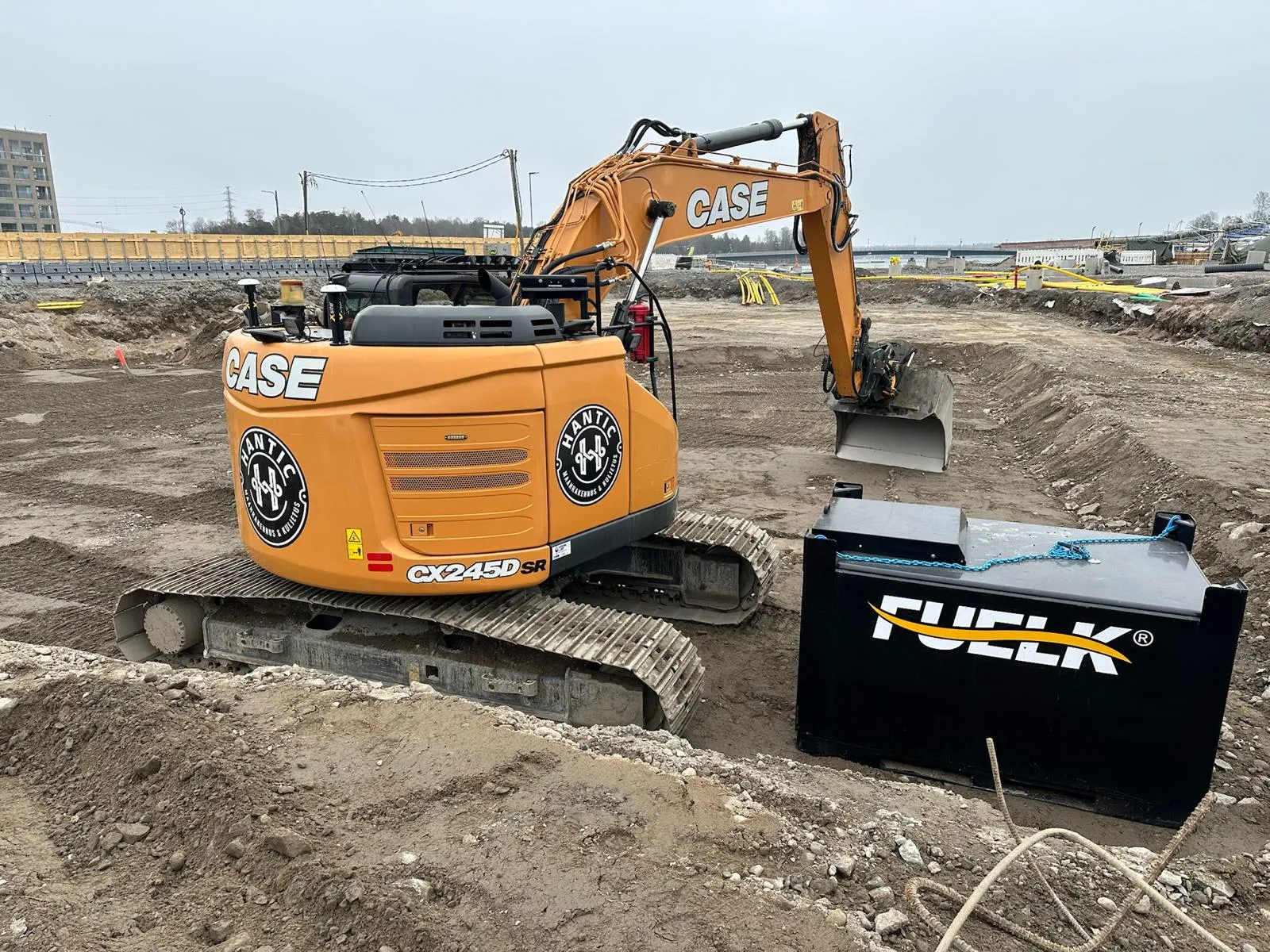 Oranssi CASE CX245D SR -kaivinkone työmaalla lähellä mustaa polttoainesäiliötä, joka on merkitty FUELK-logolla.