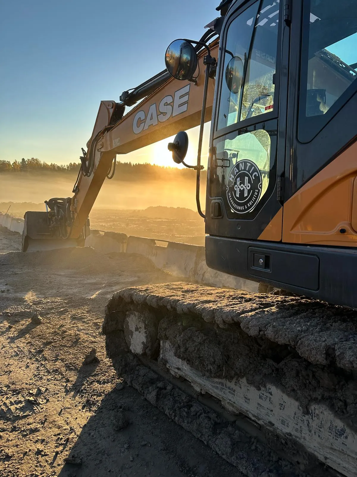 Kaivinkone työmaalla auringonlaskun aikaan, jossa näkyy CASE-merkitty varsi ja Hantic-logo ohjaamossa.