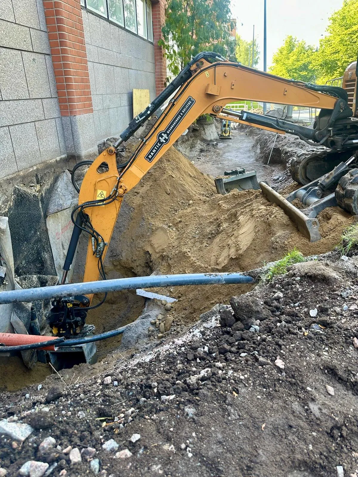 Kaivinkone kaivamassa maata rakennuksen vieressä ulkona aurinkoisena päivänä.